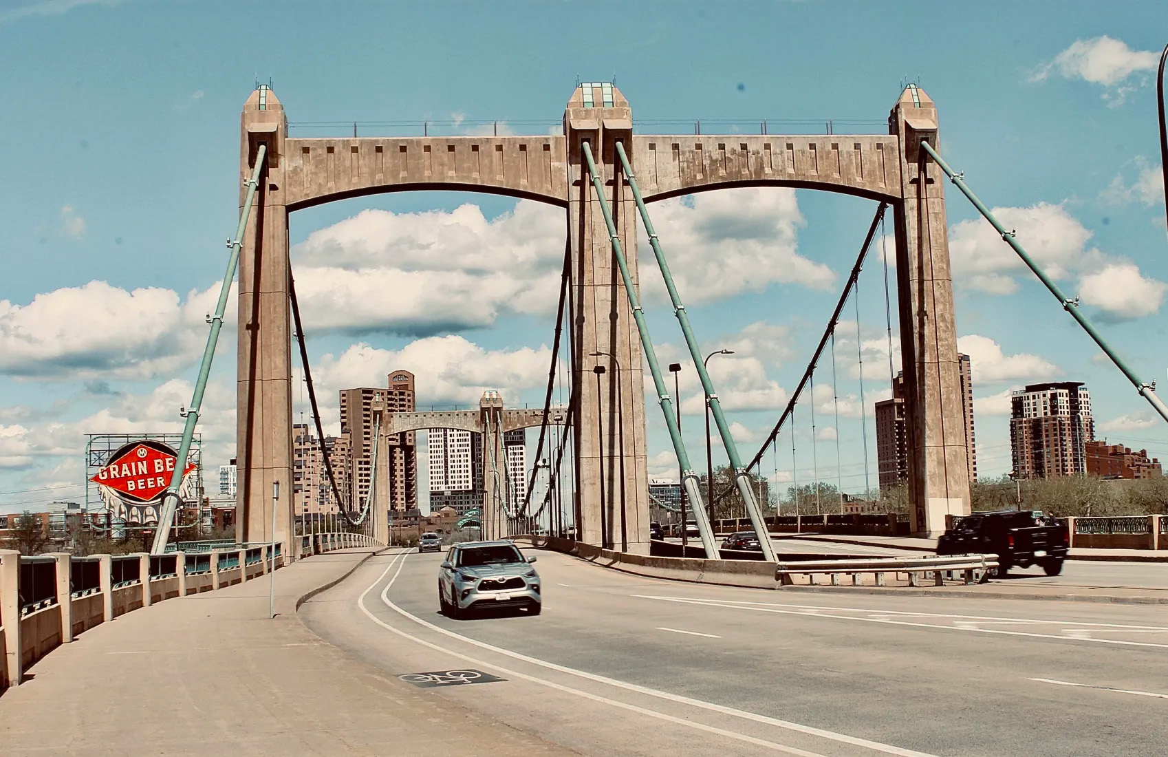 car driving under bridge near grain belt beer sign and downtown minneapolis in the background