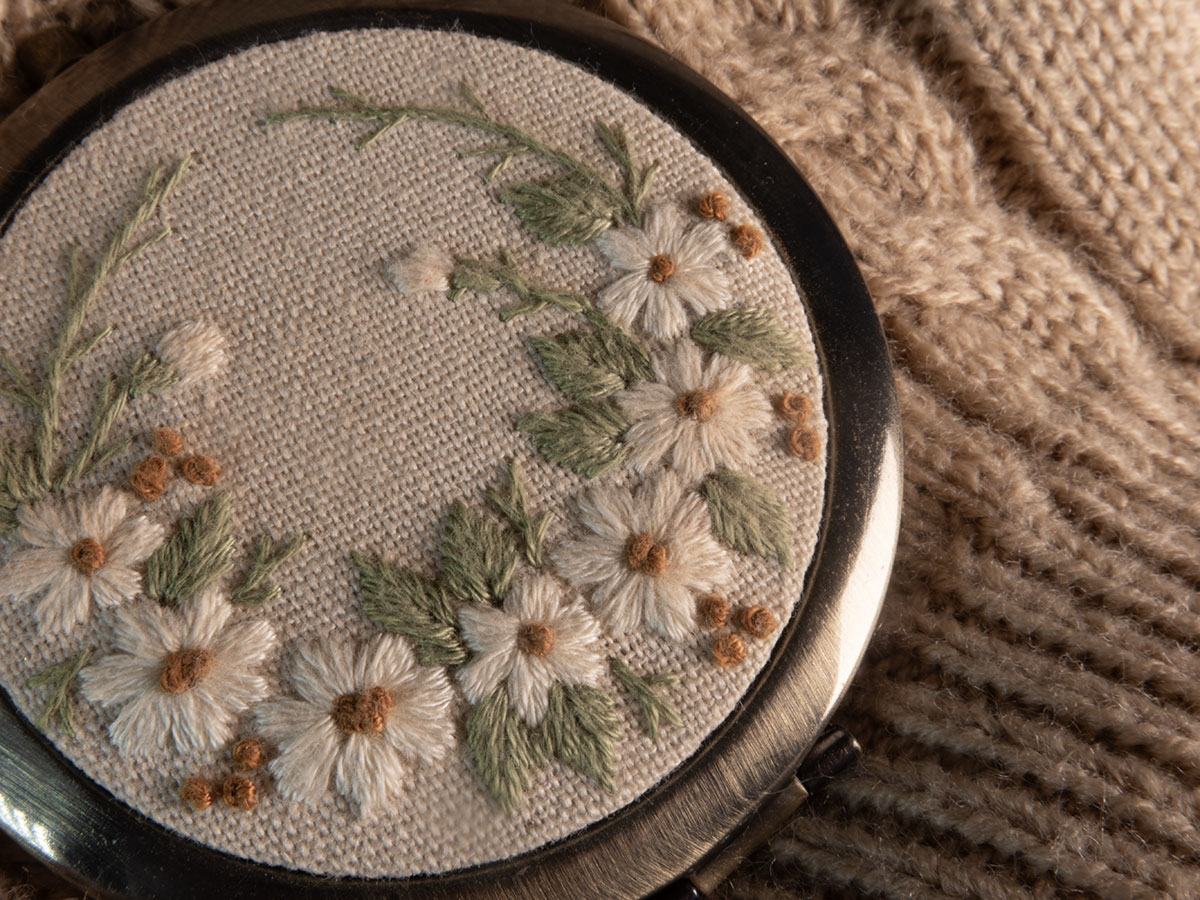 Macro photo of an small pocket mirror with embroidery on the cover laying on a knitted sweater