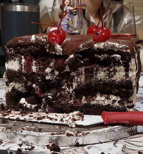 Image of a three layered chocolate cake with cherry filling, cut in half, with stabilized whipcream frosting.
