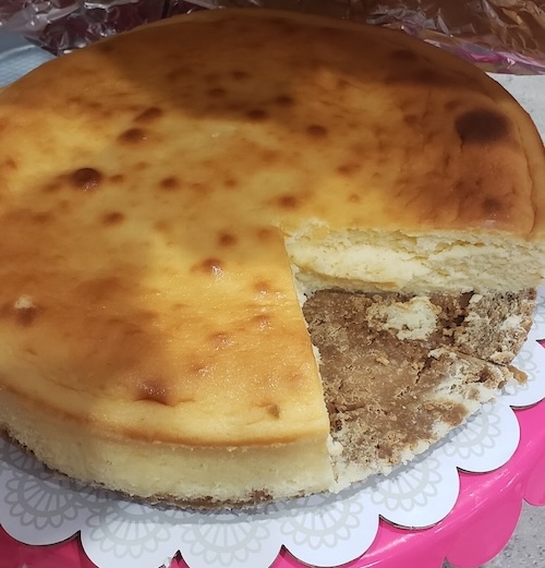 Image of a golden baked thick, round cheesecake, with a slice cut out of it.
