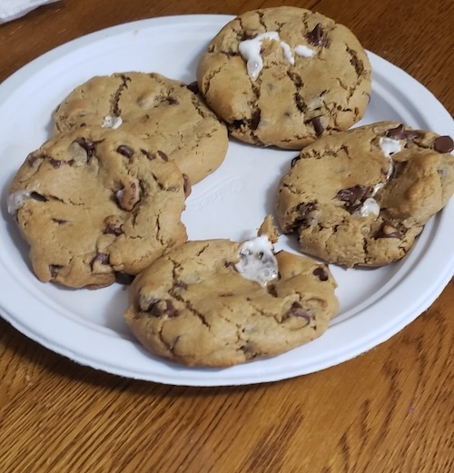 Image of thick chocolate chip cookies on a plate, bursting with marshmallow from the cracks.
