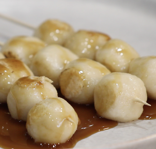 Image of three dango dough ball skewers glazed with a light brown Mitarashi sauce.